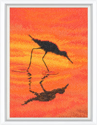 Cross-stitched artwork of a crane silhouette against an orange sunset background